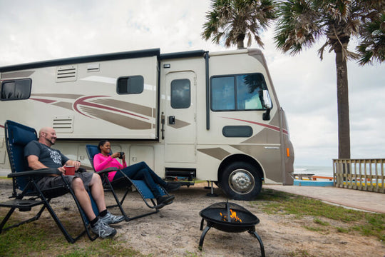 couple sits in lawn chairs in front of fire pit with their RV in the background